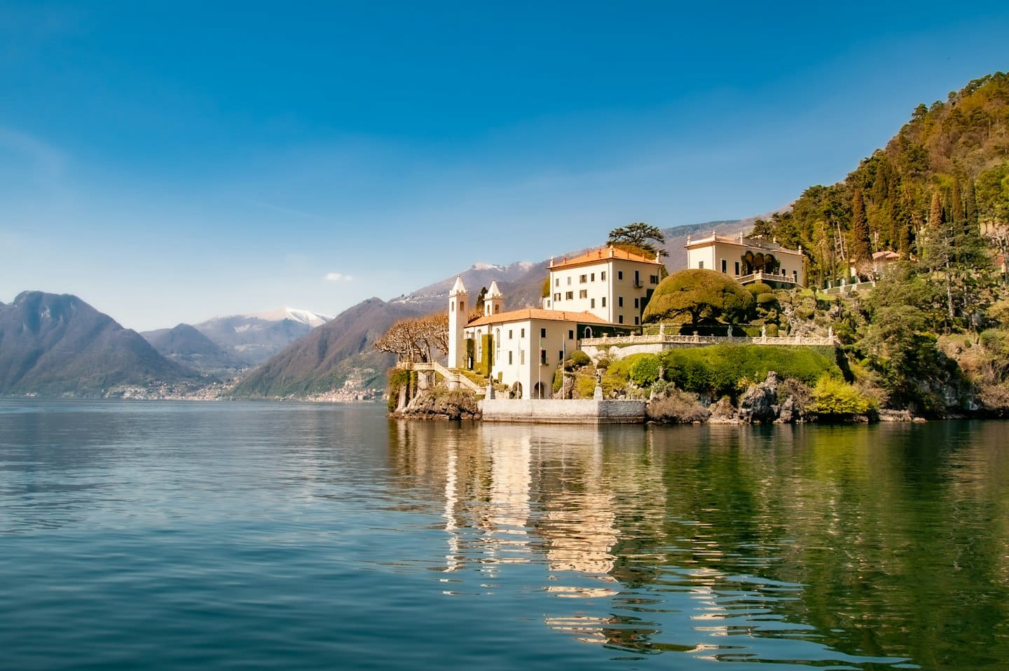 Una villa e giardini terrazzati su un promontorio roccioso che domina un lago.