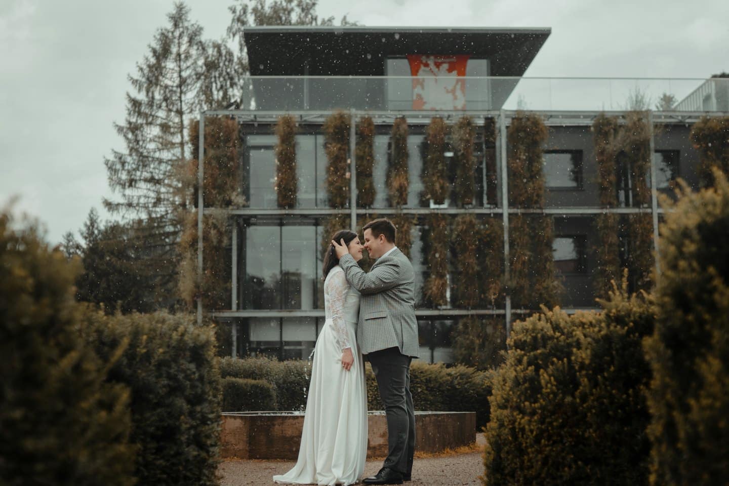 Una coppia in abiti da sposa eleganti si abbraccia in un giardino innevato.