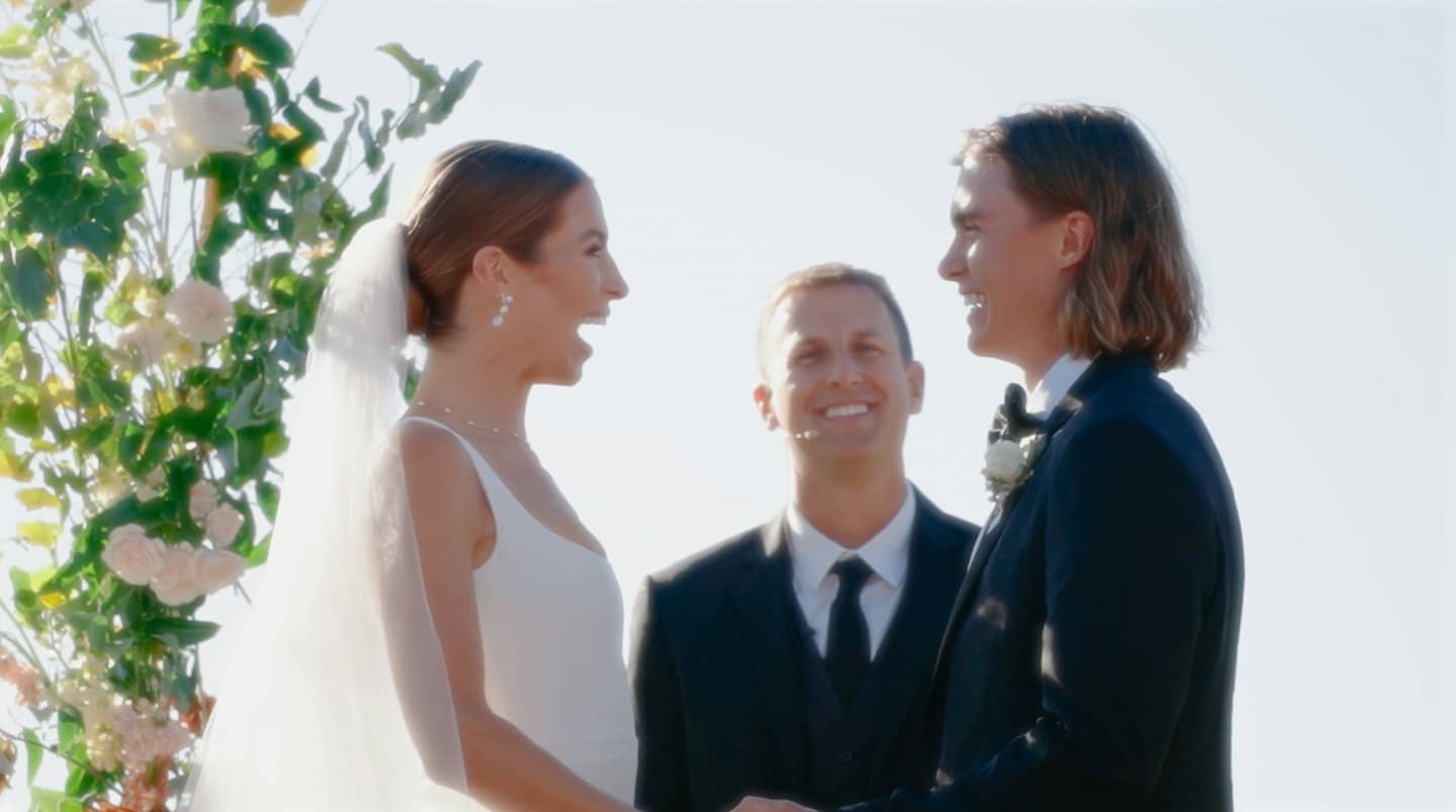 Sposi si sorridono sotto un arco floreale.